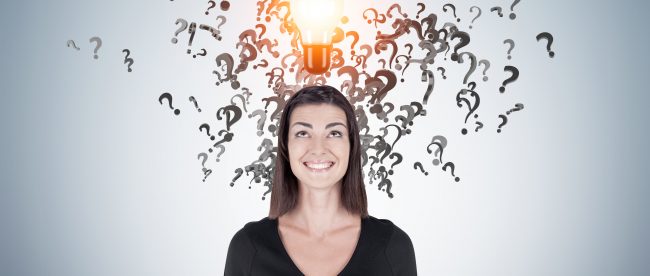 Smiling happy woman in black surrounded by question marks and a glowing light bulb above her head