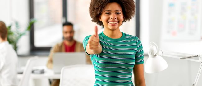 Smiling African American woman with natural hair showing a thumbs up in an office setting