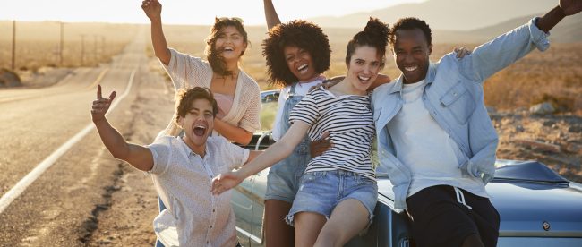 Five friends smiling next to their car on a summer road trip