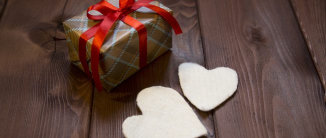 Wrapped holiday gift with golden plaid pattern wrapping and red ribbon, and two white felt hearts sitting beside gift