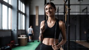 Fit woman standing in gym with skipping rope over her shoulders