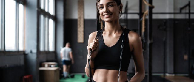 Fit woman standing in gym with skipping rope over her shoulders