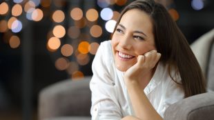 Happy woman smiling while lying on her stomach on sofa with city lights visible through the window in the background