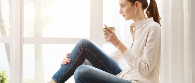 Woman quietly drinking tea beside sunny window