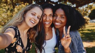 Three female friends in a park on a sunny day taking a selfie and smiling