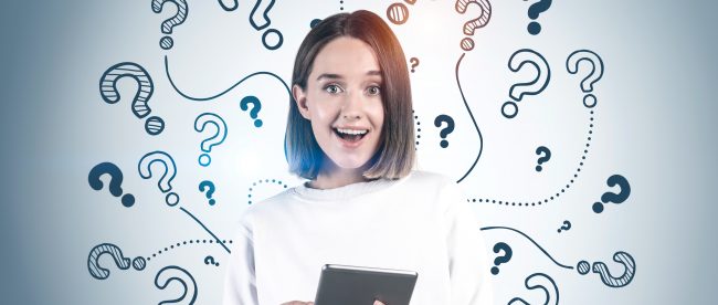 Young brown-haired woman holding a tablet while surrounded by question marks, looking excitedly at the camera