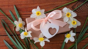 Daffodil flowers and a brown gift package with a heart-shaped tag arranged on a wooden table