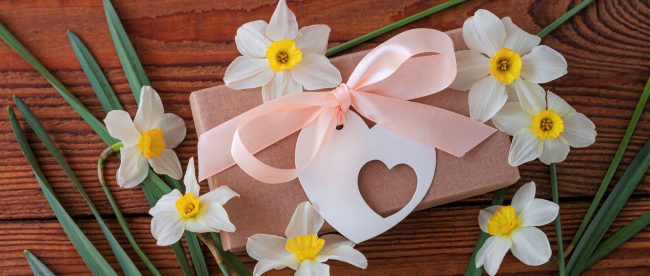 Daffodil flowers and a brown gift package with a heart-shaped tag arranged on a wooden table