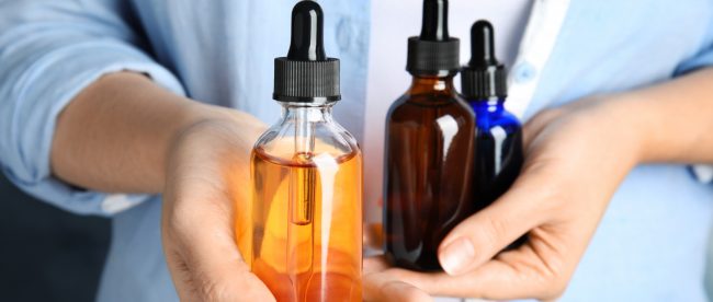 Close up of woman's hands holding large eyedropper bottles full of different colored liquids