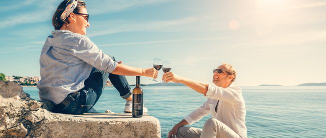 Man and woman toasting with wineglasses on rocky steps by the ocean. A nice sunny day in the fresh air.