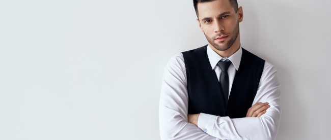 Handsome confident man in elegant suit with crossed arms on white background