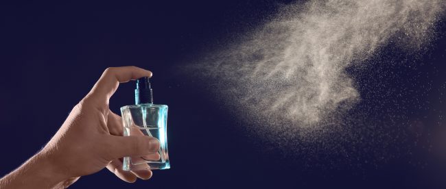 Man's hand spraying a bottle of liquid perfume against a dark blue background