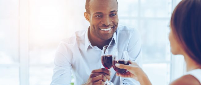Smiling man enjoying a romantic dinner with his wife, sitting at the dinner table and toasting with wine glasses
