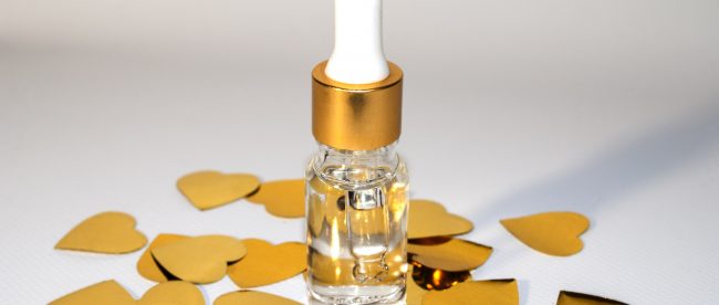 A small eyedropper bottle full of clear liquid. It is surrounded by pieces of small gold heart-shaped confetti.