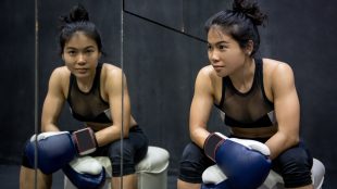 Young female boxer sitting next to a mirror, giving the camera a confident smile.