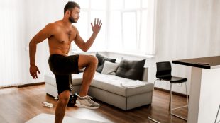 Young man working out at home, doing high steps in his living room
