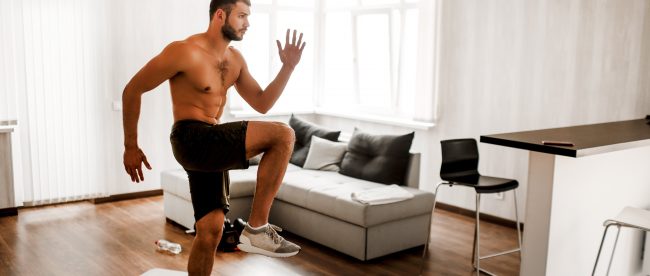 Young man working out at home, doing high steps in his living room