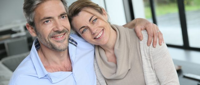 Middle-aged couple sitting together on a sofa with their arms around each other