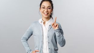 Young professional woman wearing glasses, a button down shirt, and a gray cardigan holding up one finger, prepared to teach something