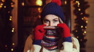 Pretty young woman bundled up for winter, with a knitted cap, scarf over her face, and gloves.