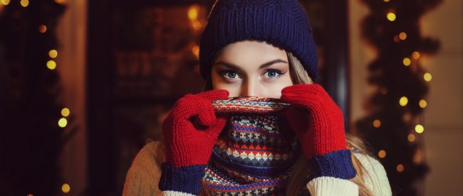 Pretty young woman bundled up for winter, with a knitted cap, scarf over her face, and gloves.