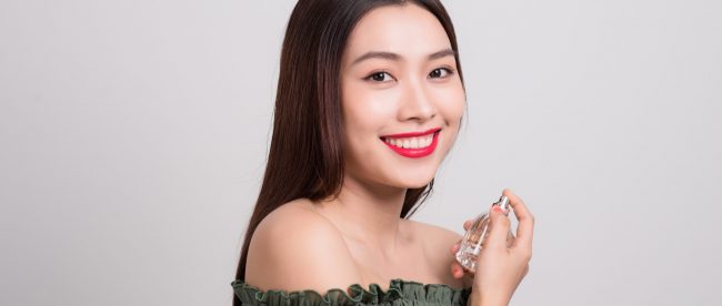 Smiling young Asian woman holding a perfume bottle