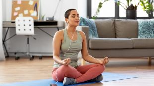 Young woman meditating in her home office while listening to music through her headphones