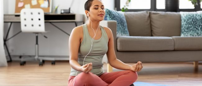 Young woman meditating in her home office while listening to music through her headphones