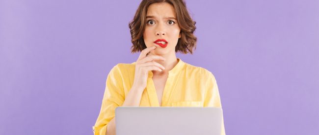 Woman holding up her laptop and biting her lip with a confused expression on her face.