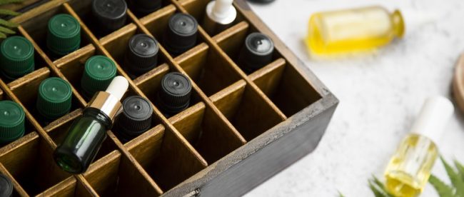 A wooden box with individual compartments for glass bottles, including dripper bottles and eyedropper bottles, holding DIY fragrances
