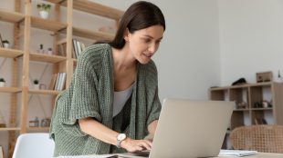 Woman working from home leaning over her laptop and enthusiastically working on something