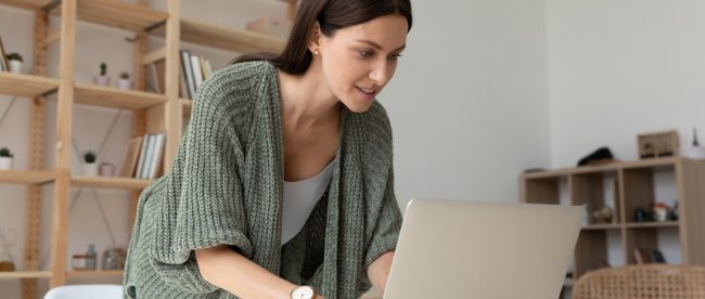 Woman working from home leaning over her laptop and enthusiastically working on something