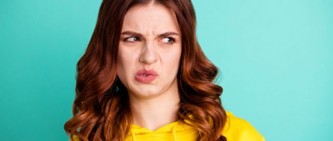 A young woman in a yellow shirt makes a face that says she smells something weird and looks off to one side out of the corner of her eye.