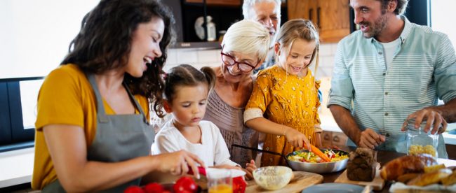 Picture of a family gathered in a kitchen, cooking a holiday meal together. Grandparents, parents, and children all cook together.