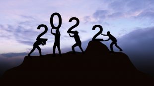 Silhouette of four people on a mountantop arragning numbers to show 2022 in celebrating of the new year