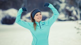 Young woman in workout gear flexing her arm muscles in a snowy park