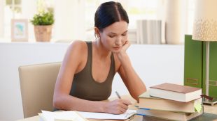 Young woman in a tank top working diligently at her desk next to a pile of books