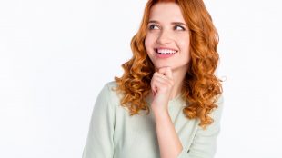 Young cirly haired redhead woman touches her chin thoughtfully and smiles