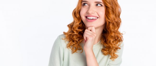 Young cirly haired redhead woman touches her chin thoughtfully and smiles