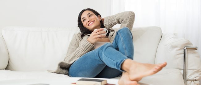 Woman relaxing on her couch with her bare feet up on her coffee table. She is smiling and thinking about something