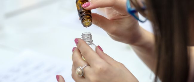 A woman carefully adds drops of liquid from one small bottle into another.