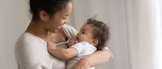 Mother holding her baby in her arms, smiling down at him happily.