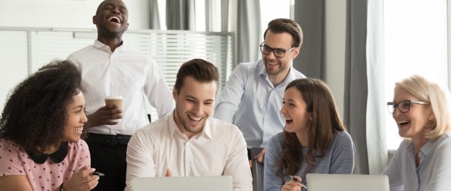 A group of friendly colleagues in an office laughing around a conference table.