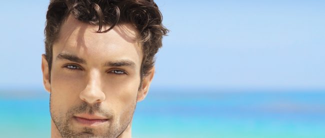 Young black-haired man with a blurry beach in the background