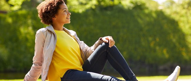 Happy woman sitting with her legs stretched out in a park in the sunshine