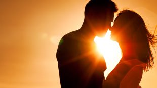 A silhouette of a couple leaning close to each other at sunset