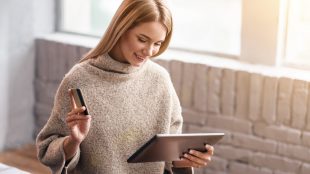 Woman in sweater doing some online shopping on her tablet, credit card in hand.
