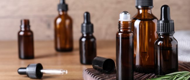 Several brown glass bottles, including both eyerdropper bottles and roll top bottles, sit on a wooden counter.