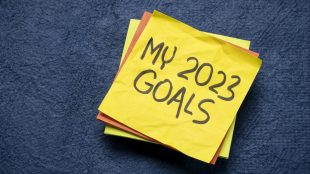 A stack of Post-It notes on a blue background. The top note is wrinkled and says "My 2023 Goals" in all capital letters.