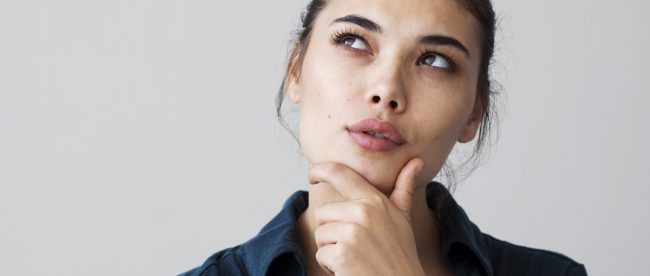 A woan in a blue shirt thinks about something while resting her chin in her hand.